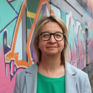 Photo of Professor Jane Farmer standing in front of a wall of graffiti
